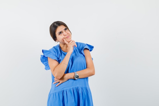 Mulher jovem de vestido azul em pose pensativa e indecisa