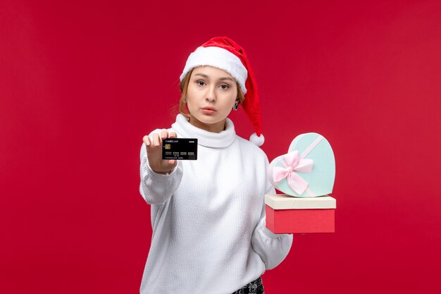 Mulher jovem de vista frontal com presentes e cartão do banco em fundo vermelho
