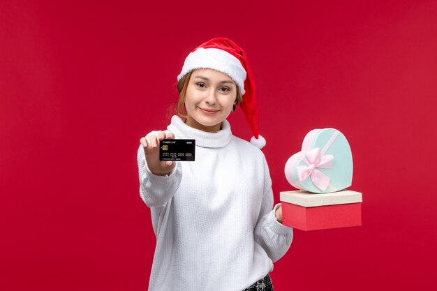 Mulher jovem de vista frontal com presentes e cartão do banco na mesa vermelha