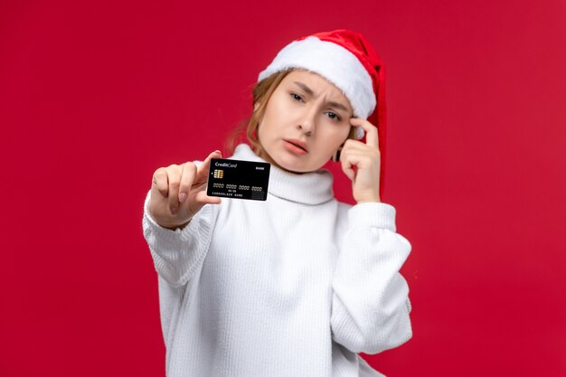 Mulher jovem de vista frontal posando com cartão do banco em fundo vermelho