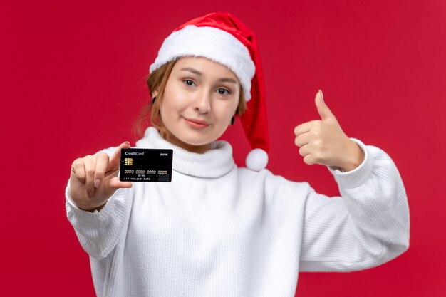 Mulher jovem de vista frontal posando com cartão do banco em fundo vermelho