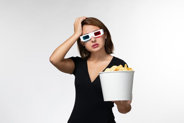 Mulher jovem de vista frontal segurando batatas fritas em óculos de sol d e assistindo filme na superfície branca