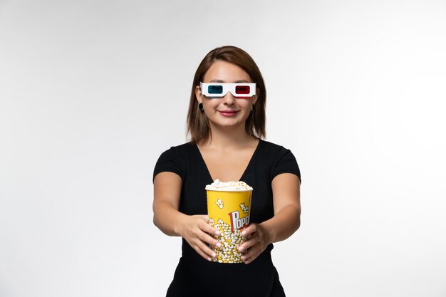Mulher jovem de vista frontal segurando pipoca em óculos de sol d assistindo filme e sorrindo na superfície branca