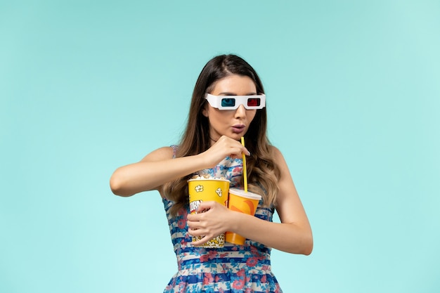 Foto grátis mulher jovem de vista frontal segurando um pacote de pipoca e bebida em óculos de sol d na superfície azul claro