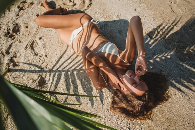 Mulher jovem deitada na praia de areia sob uma folha de palmeira