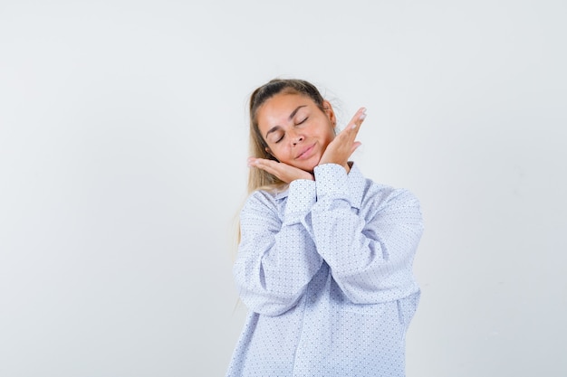 Mulher jovem descansando o rosto nas mãos, mantendo os olhos fechados, camisa branca e parecendo uma fofa