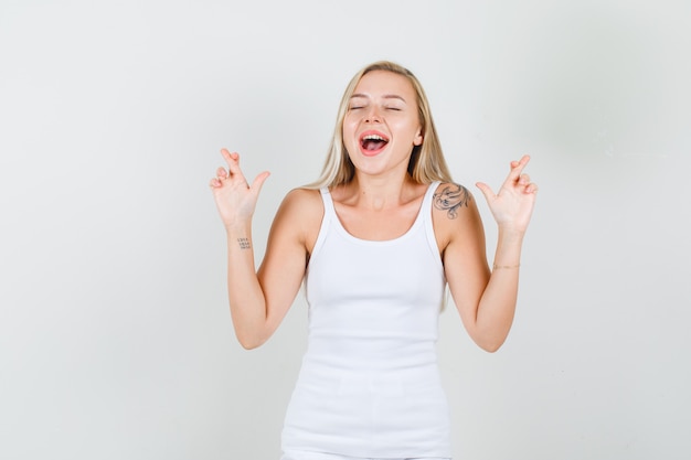 Mulher jovem desejando boa sorte com dedos cruzados em uma camiseta branca