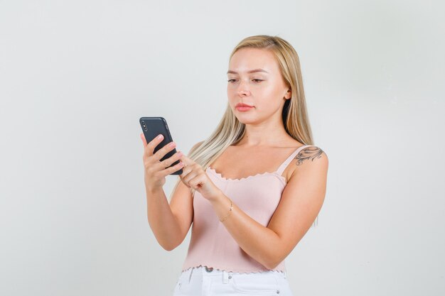 Mulher jovem digitando em um smartphone e sorrindo em camiseta