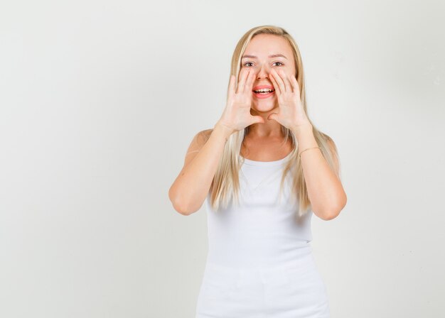 Mulher jovem dizendo algo confidencial em uma camiseta branca e parecendo alegre