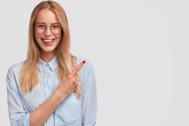 Mulher jovem e adorável feliz com sorriso gentil, manicure vermelha, apontando para o lado no canto superior direito