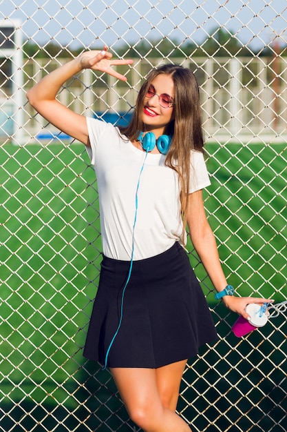 Mulher jovem e adorável hippie posando com um copo de suco saudável, ouvindo música favorita