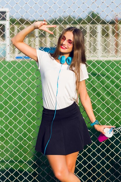 Mulher jovem e adorável hippie posando com um copo de suco saudável, ouvindo música favorita