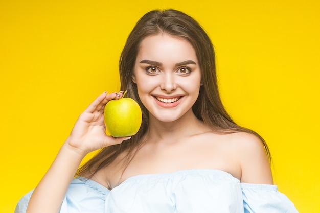 Mulher jovem e alegre com maçã, isolada em amarelo.