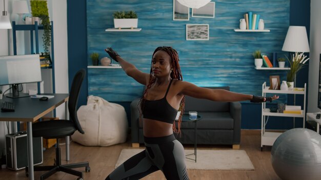 Mulher jovem e atlética de ajuste fino vestindo roupas esportivas, treino de perna, postura, sentada no mapa de ioga na sala de estar