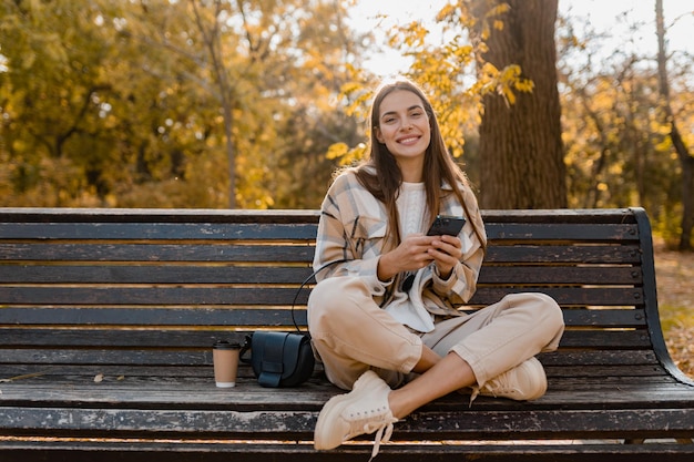 Mulher jovem e atraente andando no outono vestindo jaqueta usando telefone