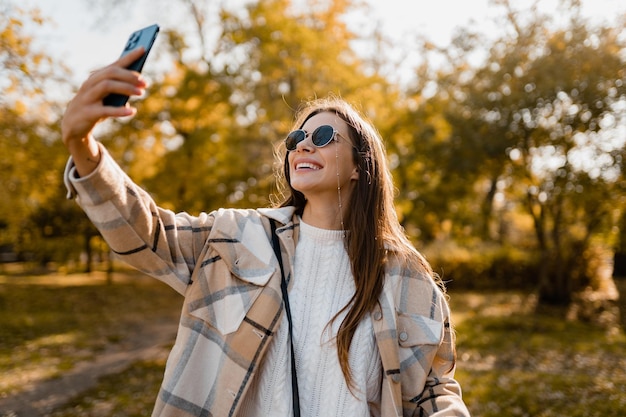 Mulher jovem e atraente andando no outono vestindo jaqueta usando telefone