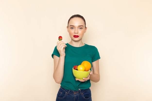 Mulher jovem e atraente de frente com camisa verde escura segurando um prato com frutas