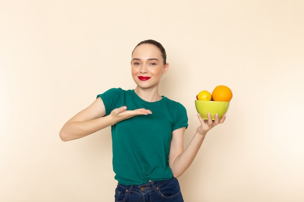 Mulher jovem e atraente de frente com camisa verde escura segurando um prato com frutas