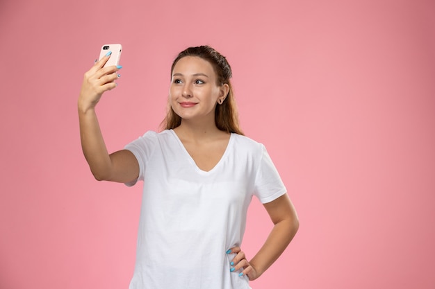 Mulher jovem e atraente de frente para a camiseta branca com um sorriso tirando uma selfie no fundo rosa