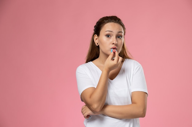 Mulher jovem e atraente de frente para uma camiseta branca, apenas posando tocando os lábios no fundo rosa