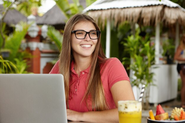 Mulher jovem e atraente de óculos, parecendo alegre enquanto faz videochamada para a amiga