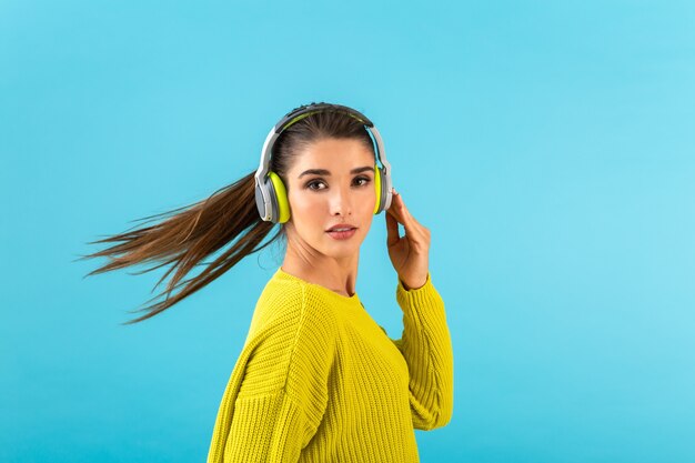 Mulher jovem e atraente e elegante ouvindo música em fones de ouvido sem fio, feliz, vestindo uma blusa de malha amarela