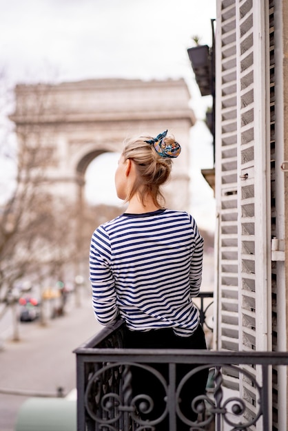 Foto grátis mulher jovem e atraente na varanda de manhã na cidade de paris. vista do arco triunfal.