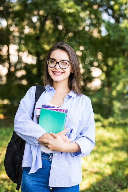Mulher jovem e atraente sexy com livros em pé e sorrindo no parque