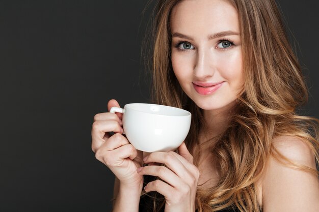 Mulher jovem e atraente sorridente segurando copo branco e bebendo café