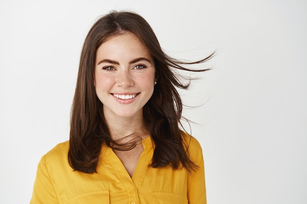 Mulher jovem e atraente sorrindo, sentindo-se saudável, cabelo voando no vento