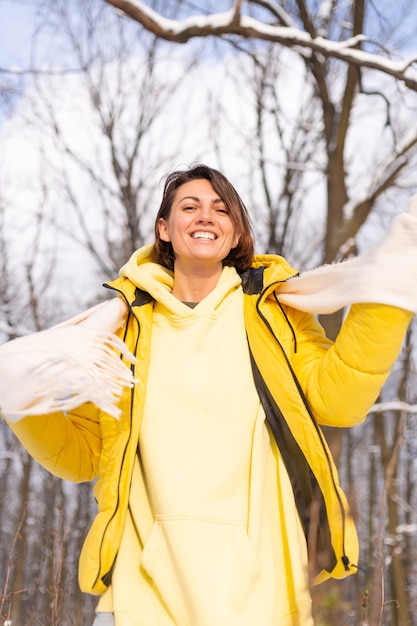 Mulher jovem e bonita alegre em uma floresta de inverno com neve, se divertindo, se alegra no inverno e neve em roupas quentes