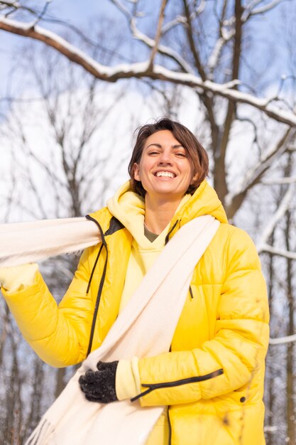 Mulher jovem e bonita alegre em uma floresta de inverno com neve, se divertindo, se alegra no inverno e neve em roupas quentes