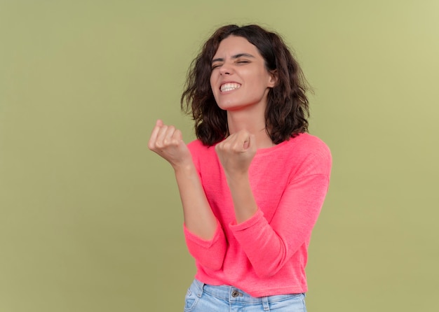 Mulher jovem e bonita alegre levantando os punhos na parede verde isolada com espaço de cópia