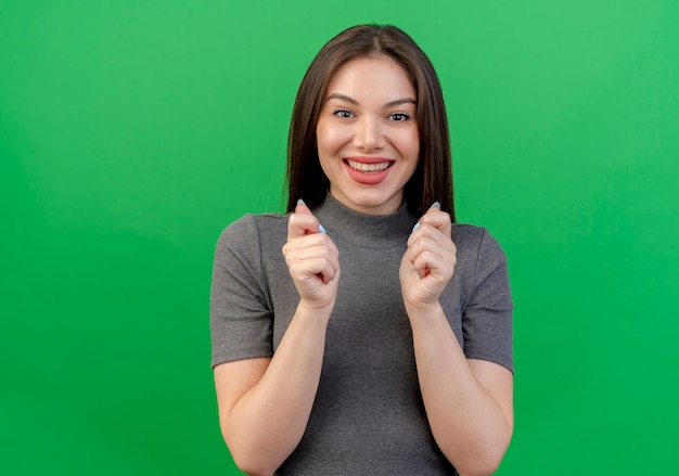 Foto grátis mulher jovem e bonita animada cerrando os punhos e implorando por algo isolado em um fundo verde com espaço de cópia