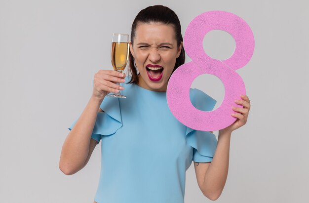 Mulher jovem e bonita animada segurando o número oito rosa e uma taça de champanhe