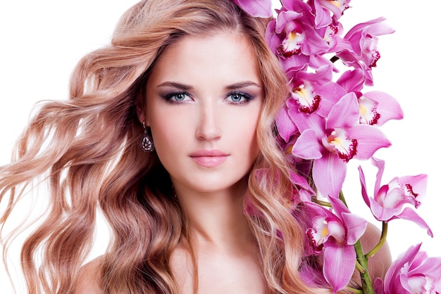 Mulher jovem e bonita bonita com uma pele saudável e flores cor de rosa perto do rosto - isolado no branco.