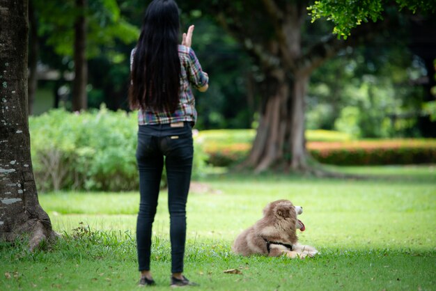 Mulher jovem e bonita brincando com seu cachorro pequeno em um parque ao ar livre. Retrato do estilo de vida.