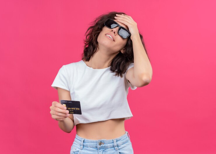 Foto grátis mulher jovem e bonita cansada usando óculos escuros e segurando um cartão, colocando a mão na testa em uma parede rosa isolada com espaço de cópia