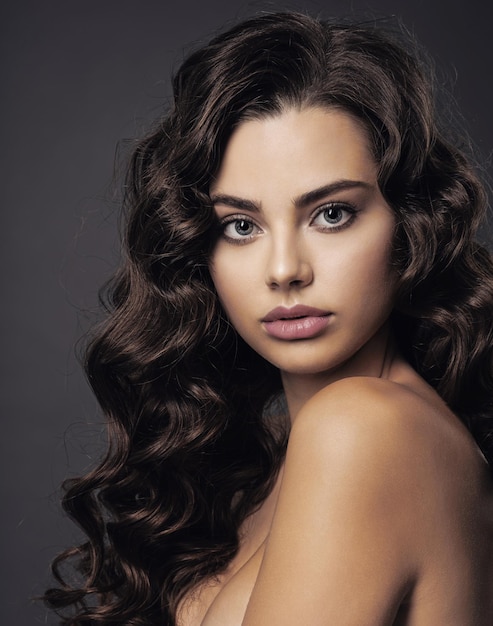 Mulher jovem e bonita com cabelo castanho longo encaracolado e maquiagem esfumada nos olhos. menina morena sexy e linda com um penteado ondulado. retrato de uma mulher atraente. modelo de moda.