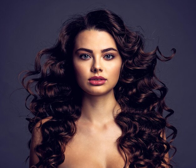 Mulher jovem e bonita com cabelo castanho longo encaracolado e maquiagem esfumada nos olhos. Menina morena sexy e linda com um penteado ondulado. Retrato de uma mulher atraente. Modelo de moda.