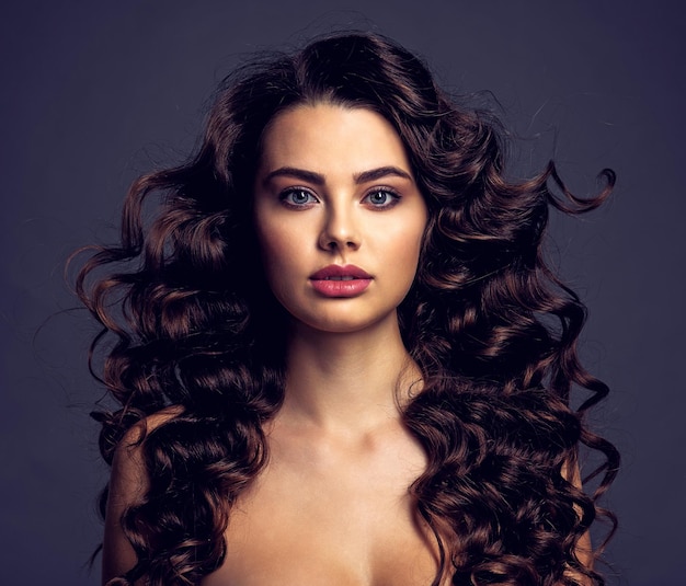 Mulher jovem e bonita com cabelo castanho longo encaracolado e maquiagem esfumada nos olhos. Menina morena sexy e linda com um penteado ondulado. Retrato de uma mulher atraente. Modelo de moda.