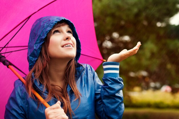 Mulher jovem e bonita com capa de chuva e guarda-chuva para verificar se há chuva