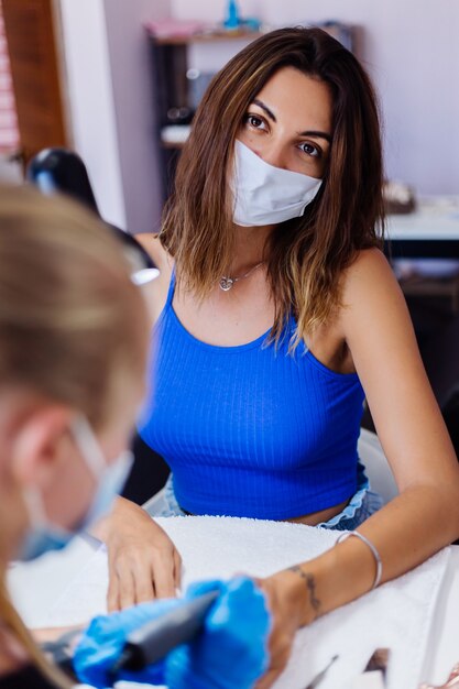 Mulher jovem e bonita com máscara médica protetora em salão de beleza de unhas com luz suave natural incrível