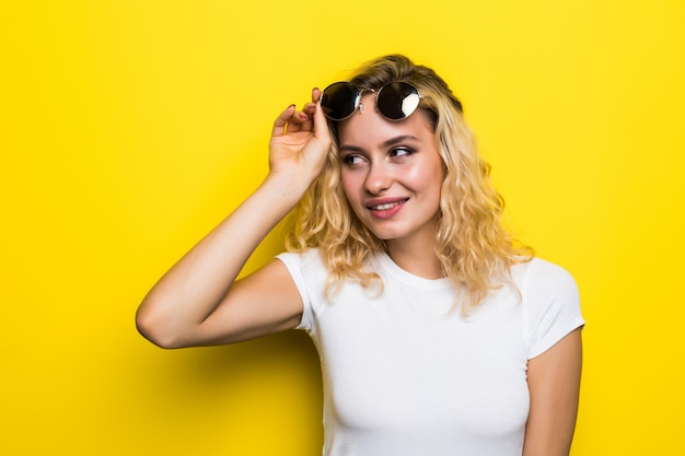 Mulher jovem e bonita com óculos de sol na parede amarela