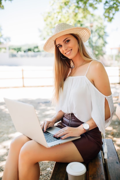 Mulher jovem e bonita com um laptop em um banco de jardim