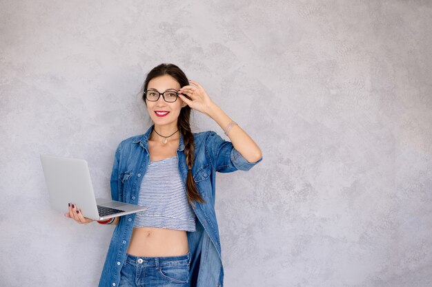 Mulher jovem e bonita de óculos em pé com um laptop nas mãos dela