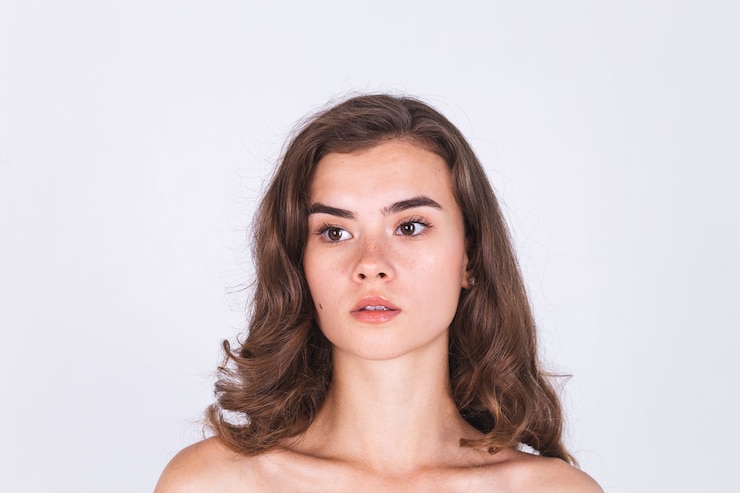 Foto grátis mulher jovem e bonita de pele limpa, natural, com sardas, maquiagem leve na parede branca e ombros nus