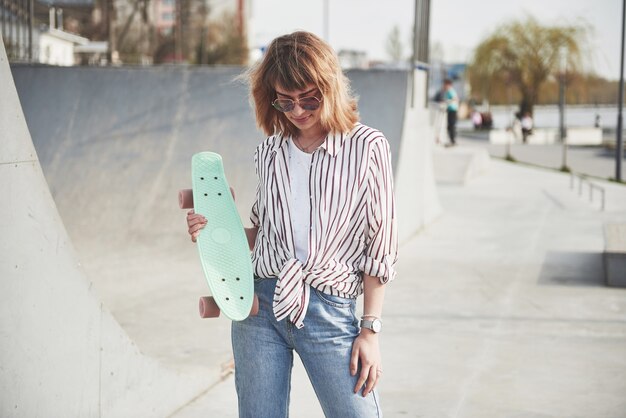 Mulher jovem e bonita elegante com um skate, em um lindo dia ensolarado de verão.