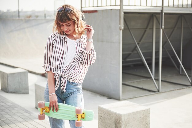 Mulher jovem e bonita elegante com um skate, em um lindo dia ensolarado de verão.