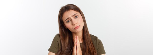 Mulher jovem e bonita em roupas casuais juntos de mãos dadas e rezando isolado no branco